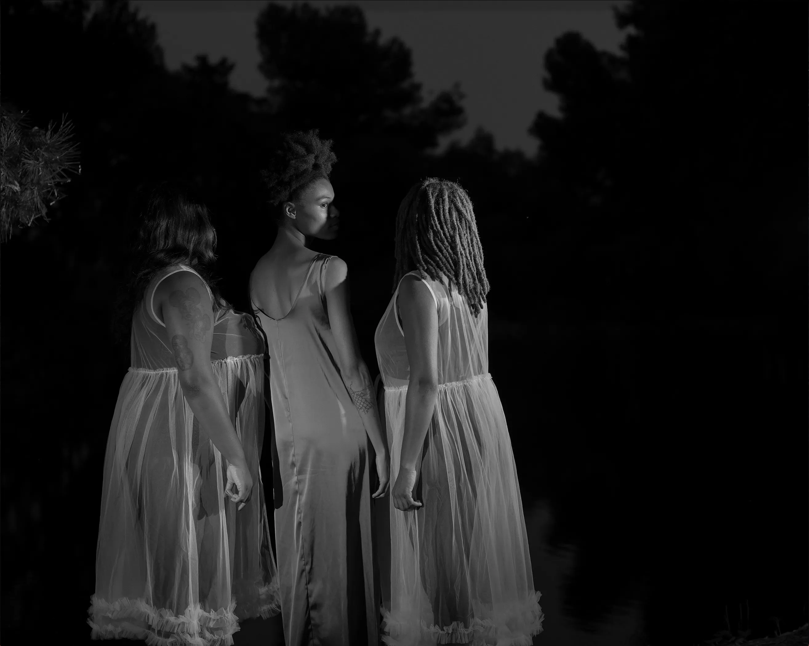 three black women stand together in white dresses